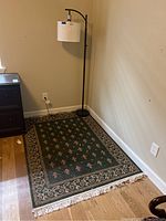 Photo showing the green area rug with floral and geometric patterns next to the black curved tall floor lamp against a beige wall.