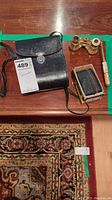 Top view of three vintage binoculars and a carrying case on a wooden table with a green border and a tag number 489.