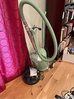 Green canister vacuum with flexible hose and wheels, electrical cord visible.