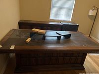 Photo showing wood desk with glass inset top and decorative paneling on front, some objects on desk surface.