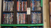 Two rows of DVDs and Blu-rays on black shelving unit showing various titles and covers.