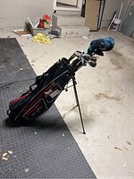 Golf clubs inside a black and red golf bag with stand legs extended.