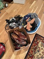 Image showing a box with brown leather dress shoes with shoe trees inside and a pair of Adidas tennis shoes underneath. Nearby is a laundry basket with a Texas Rangers cap, cedar hangers, and shoe trees.