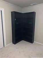 Two black IKEA Billy bookcases arranged together in an L shape in an empty room with light colored carpet and beige walls.