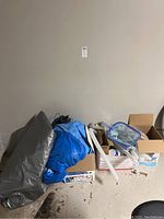 Photo showing various pool-related items including an inflatable ring, a zippered mesh pool skimmer, and boxes containing other pool accessories. Items are stored on the floor needing cleaning.
