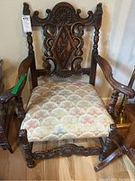 Front view of wooden side chair showing ornate carvings on backrest, padded fabric seat, and armrests.