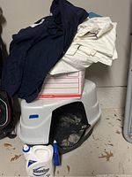 Photo showing a white cat litter box with black mesh, folded dark blue and off-white sheets, and a box stacked together
