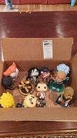 Top-down view of 11 unpackaged bobblehead figures in a cardboard box showing a variety of characters from pop culture and sports.