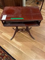 Front view of the wooden side table showing the top, storage shelf and carved legs with metal feet.