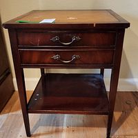 Front view of mahogany side table showing two drawers with decorative handles and the leather inlaid top with wear marks and scratches.