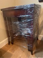 Full view of the wood side table wrapped in plastic showing the legs and drawer front.