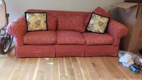 Front full view of red upholstered sofa with three seat cushions and floral pillows.