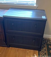 Front view of the two drawer file cabinet showing wood grain texture, two drawers with round knobs, and some wear marks on the surface.