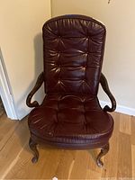Front view of one dark brown leather office chair with tufted seat and back, wooden armrests and cabriole legs