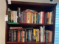 Books on two shelves showcasing a mix of paperback and hardback books in worn condition, ranging across several genres including sports, mysteries, self help, and short stories.