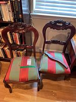 Pair of wooden chairs with carved floral backs and striped upholstered seats, one chair leg detached and placed on seat.