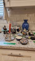 Photo showing the blue swirling vase, metal and wood duck sculpture, silverplated candleholder with candle, Star Wars and Avengers collectible glasses, and Asian inspired pottery pieces on countertop.