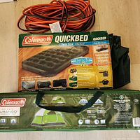 Photo showing coiled orange extension cord, Coleman QuickBed Twin Size air mattress box, and Coleman Durango 4-person tent in carrying case.