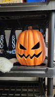 Orange jack-o'-lantern pumpkin decoration with carved face on black shelf.