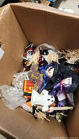 Open cardboard box showing a variety of Halloween figurines including a ghost, witches, and a pirate skeleton figure.