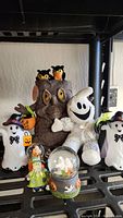 Photo showing a group of Halloween decorations including ghost figures, owl tree, witch and ghost figurines, and a snow globe.