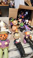 Photo of small Halloween figurines including pumpkin-headed figure, owl, witch and assorted small characters in front of and around an open box