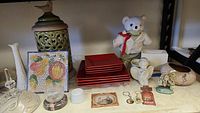 Shelf with various used decorative items, plates, plush teddy bear, ceramic jars, and small sculptures arranged for review.