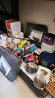 Photo showing a variety of cat supplies including bowls, toys, containers, and mats in used condition.