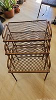 Top view of 3 rust-colored metal mesh nesting tables stacked together showing rectangular tops with diamond pattern mesh and side handles.