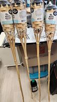 Four Tiki bamboo torches standing upright, each with sealed torch fuel bottle attached at the base.
