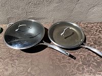 Photo showing 2 Calphalon non-stick pans side by side on a patterned fabric surface, including a 13-inch wok with glass lid and a 13-inch fry pan.