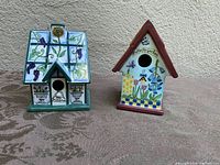 Front view of both birdhouse figurines showing detailed decorative designs and birdhouse openings.