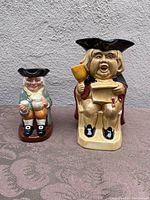 Frontal view of two Toby jugs showing character details, colors, and posture