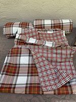 Three rolled up Eddie Bauer duvet covers and one unfolded cover showing red, white, brown plaid and checkered patterns