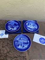 Three blue and white Royal Copenhagen Christmas plates from 1997-1999 displayed on boxes with certificates.