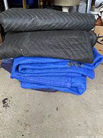 Stack of six moving blankets, black and blue, with visible tears and wear.