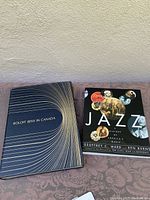 Two books shown side by side on a surface: Roloff Bennys Canada hardcover with black and white cover design and Jazz A History of American Music softcover with photographic collage cover.