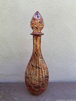 Full view of tall slender Bombay art glass genie bottle with swirled orange and black glass pattern and matching stopper.