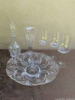 Full lot displayed showing the crystal decanter with stopper, trumpet vase, decorative bowl and three Bordeaux wine glasses arranged on a dark cloth.