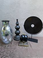 Full view of all four items in the lot: mercury glass vase, ceramic finial, round metal disc sculpture, and decorative bookends.
