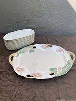 Stack of 10 rectangular ceramic plates shaped like corn on the cob, cream colored with textured surface. Fitz & Floyd floral platter with two handles and floral pattern visible in front.