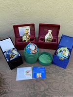 All five boxed glass Christmas ornaments displayed on a surface, showing their boxes and decorative designs.