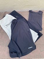 Four men's clothing items laid out: two Lululemon shorts (dark navy and light beige), one Patagonia black shorts, and one folded Lululemon dark gray shirt.