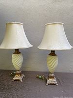 Pair of cream-colored table lamps with twisted crackle ceramic bodies and distressed metal bases with damask lampshades, photographed against a gray wall.