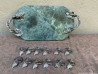 Full view of green marble cheese board with ornate pewter grape cluster handles and set of 12 matching pewter napkin rings in front.