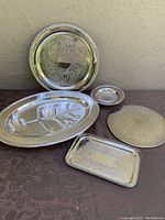 Five silver plate trays and dishes of different shapes and sizes displayed together showing overall condition and variety.