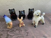 Lot of six vintage ceramic figurines including three black Shafford cat creamers, one cream Shafford sugar cat, Copley bird figurine, Pendelfin Picnic Midge rabbit, and Trentham Artware poodle figurine on a table