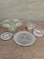 Full view of all items on table against a wall: 12-inch cake stand, swan dish, round cake plate, two ashtrays