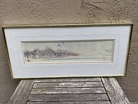 Full framed watercolour painting showing the full landscape and frame on an outdoor wooden table.