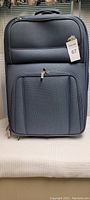 Front view of the medium sized light blue suitcase showing front pocket, main zipper and top handle.